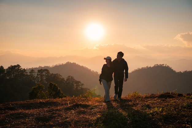 Silhueta jovem casal asiático abraçando desfrutando na colina no campo ao pôr do sol