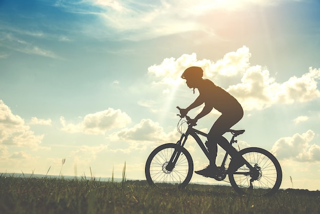 Silhueta jovem de andar de bicicleta no fundo por do sol