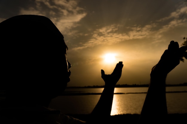 Silhueta jovem muçulmano asiático rezando no pôr do sol conceito do festival do Ramadã