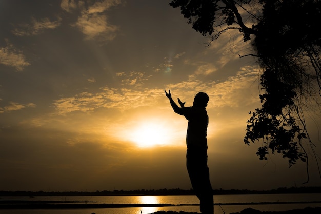 Silhueta jovem muçulmano asiático rezando no pôr do sol conceito do festival do Ramadã
