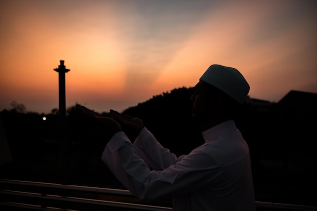 Silhueta jovem muçulmano asiático rezando no pôr do sol conceito do festival do ramadã