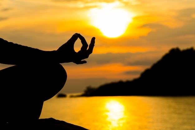 Foto silhueta, mão de mulher meditando em yoga pose ou lotus position at sunset