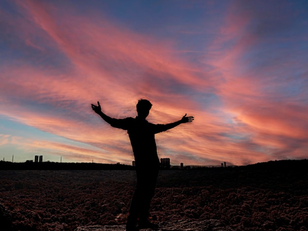 Foto silhueta de mujer con los brazos extendidos de pie contra el cielo durante la puesta de sol