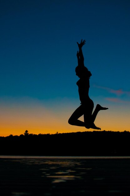 Foto silhueta de mujer con los brazos levantados saltando sobre la playa contra un cielo despejado