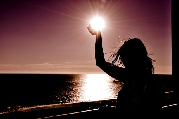 Foto silhueta de mujer por el mar contra el cielo durante la puesta de sol