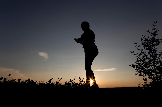 Foto silhueta de una mujer de pie en el campo contra el cielo durante la puesta de sol