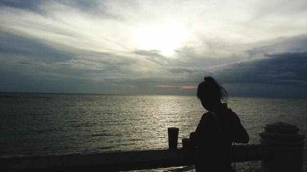 Foto silhueta de una mujer de pie contra el mar durante la puesta de sol