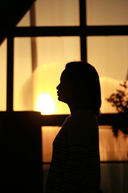 Foto silhueta de una mujer de pie contra la ventana al atardecer