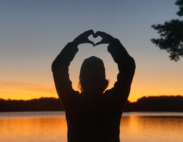 Foto silhueta de mujer de pie en forma de corazón en el lago contra el cielo durante la puesta de sol