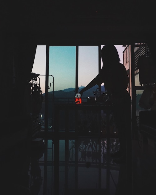 Foto silhueta de una mujer de pie junto a la ventana contra el cielo