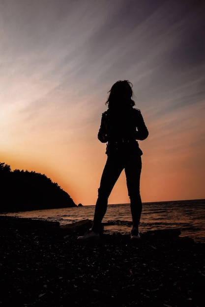 Foto silhueta de una mujer de pie en la playa durante la puesta de sol
