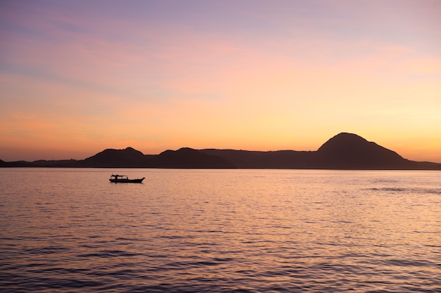 Silhueta negra de colinas com barco de pesca tradicional navegando no mar em Labuan Bajo