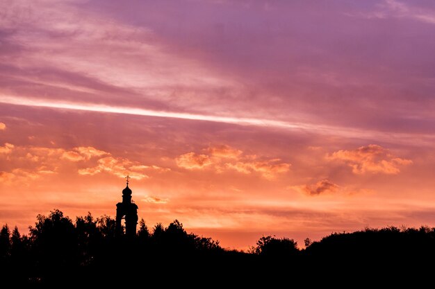 Silhueta negra do horizonte da igreja e da floresta no céu do pôr do sol roxo-dourado com nuvens suaves