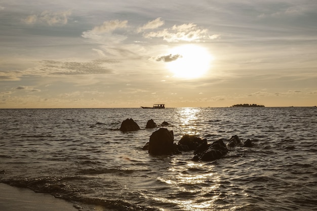 Silhueta negra e reflexo do sol no mar durante o pôr do sol com barco à vela