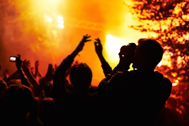 Foto silhueta de personas y cámara con multitud en un festival de música o concierto para imágenes redes sociales o artículo de noticias fotógrafo o persona oscura con naranja brillante e iluminación para una actuación de rock