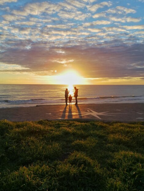 Foto silhueta de personas de pie en la playa contra el cielo durante la puesta de sol