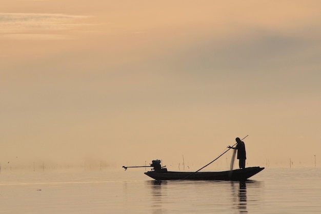 Silhueta de un pescador navegando en el mar contra el cielo durante la puesta de sol