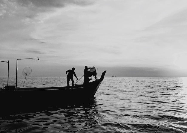 Foto silhueta de un pescador de pie en un barco en el mar
