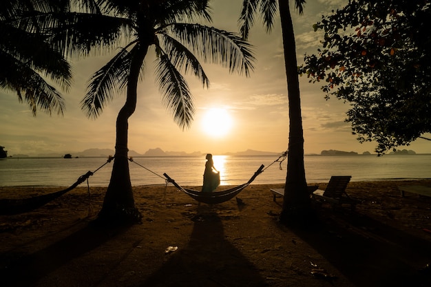 Silhueta sol matinal praia, coqueiro com rede, mulher relax