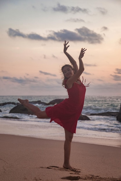 Silhueta vista traseira mulher magra de vestido vermelho com os braços levantados dançando na praia do oceano ao fundo do sol Senhora na praia do mar nas férias de verão