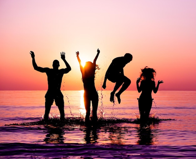 Silhuetas de amigos en el mar contra el cielo durante la puesta de sol