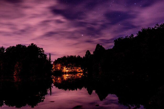 Foto silhuetas de árvores ao lado do lago contra o céu ao pôr-do-sol