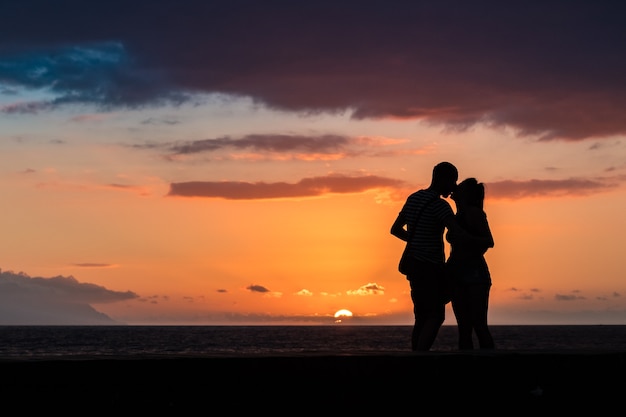 Silhuetas de casal apaixonado se beijando ao pôr do sol