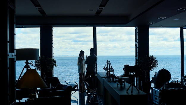 Silhuetas de colegas de trabalho discutindo projeto na janela panorâmica do oceano Vida de luxo