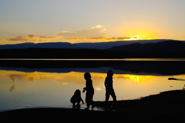 Silhuetas de crianças felizes brincando no lago na hora do pôr do sol, Reservatório Amphoe Wang Saphung Loei Tailândia