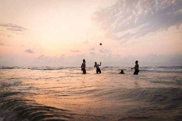 Silhuetas de crianças tendo tempo feliz na praia do mar perto do pôr do sol