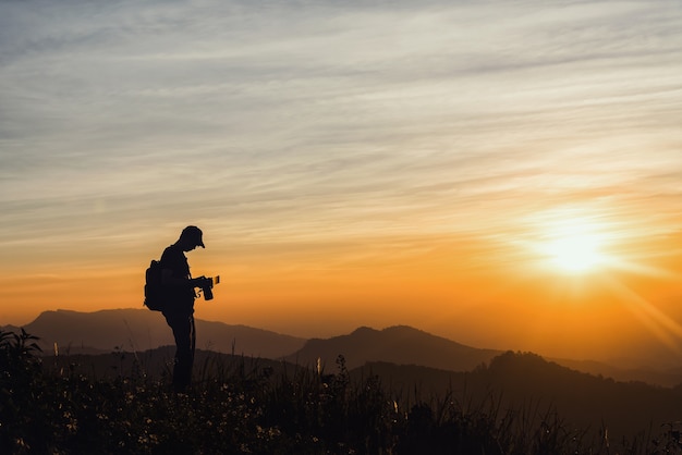 Silhuetas de fotógrafo no penhasco contra o céu de Crepúsculo colorido