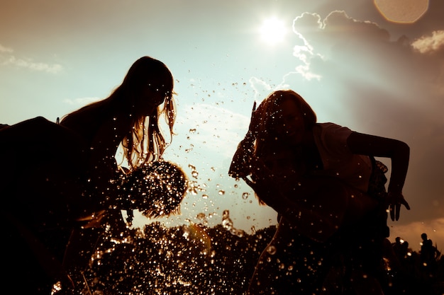 Silhuetas de meninas brincando na água contra o sol