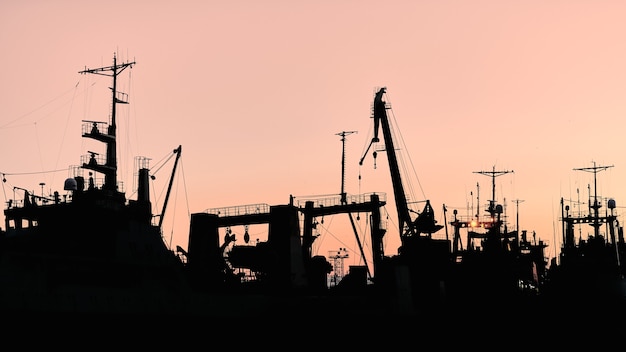 Silhuetas de navios e guindastes de contêiner no porto marítimo, plano de fundo por do sol. Paisagem industrial do cenário.