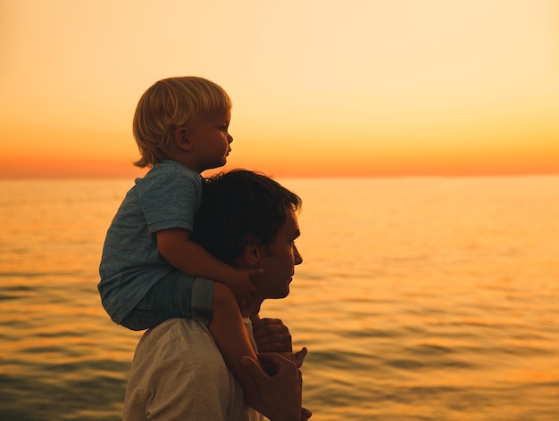 Silhuetas de pai e filho no céu pôr do sol Família amorosa e férias de verão Homem e criança menino brincando juntos ao ar livre em uma praia do mar Pai carregando criança nas costas na natureza