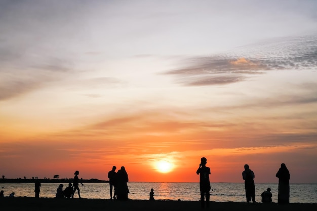 Silhuetas de pessoas tirando fotos na praia com uma silhueta de fundo por do sol de amigos