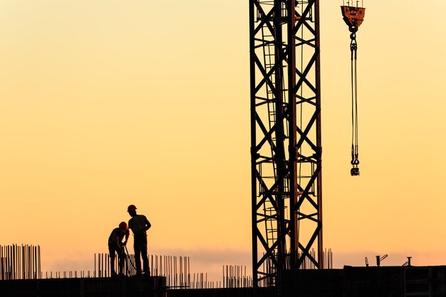 Silhuetas de trabalhadores na construção de um arranha-céu com o céu ao pôr do sol como pano de fundo