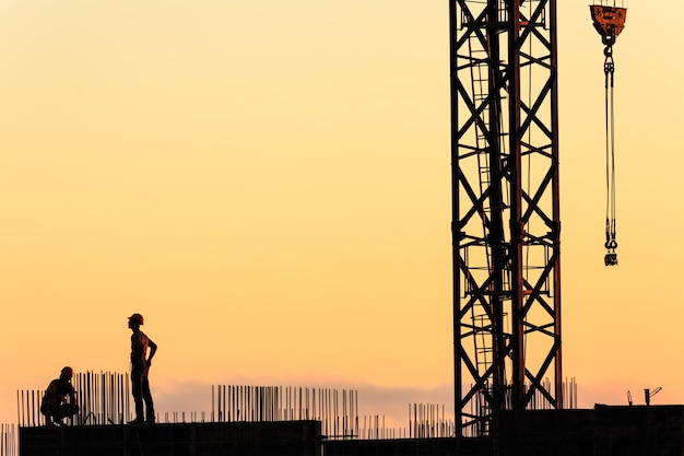 Silhuetas de trabalhadores na construção de um arranha-céu com o céu ao pôr do sol como pano de fundo