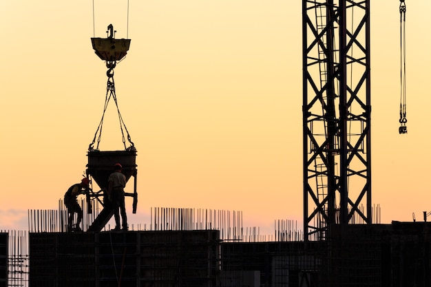 Silhuetas de trabalhadores na construção de um arranha-céu com o céu ao pôr do sol como pano de fundo