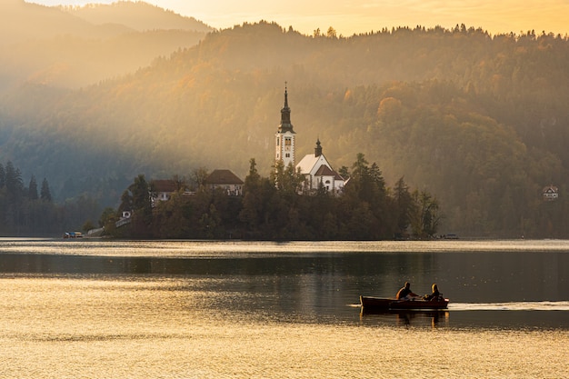 Silhuetas de um casal flutuando em um barco perto da ilha bled na bela luz do sol