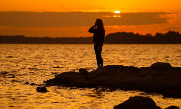 Silhuette de mujer al atardecer de pie sobre una roca mirando directamente Concepto de naturaleza y belleza Puesta de sol naranja