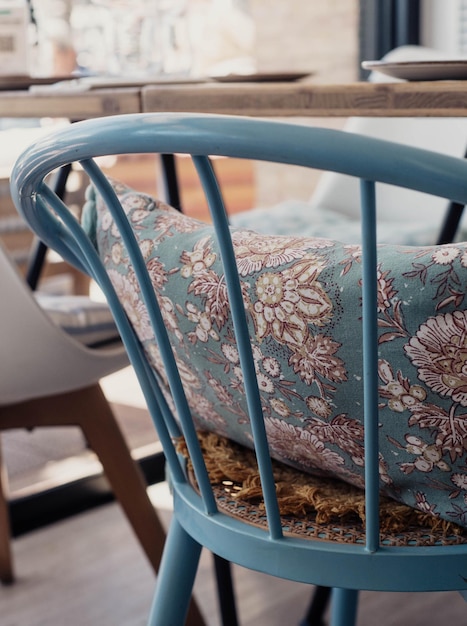 Una silla azul con una almohada floral se sienta en una habitación con una silla blanca.