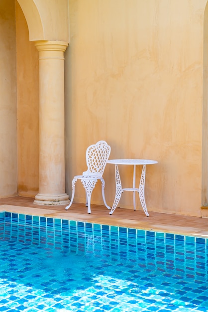 silla blanca vacía y mesa al lado de la piscina