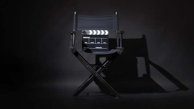 Silla de director negra y tablero de chapaleta o claqueta de cine sobre fondo negro.Uso en producción de video o industria cinematográfica