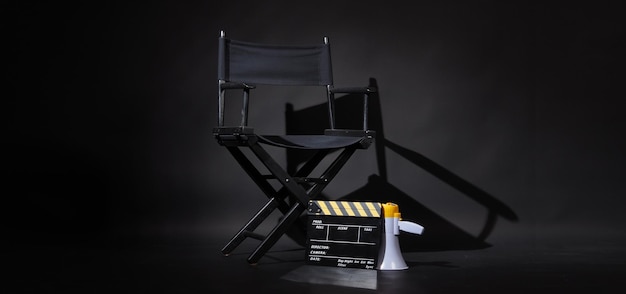 Silla de director negra y tablero Clapper o Clapperboard de película con megáfono sobre fondo negro Uso en producción de video o industria cinematográfica