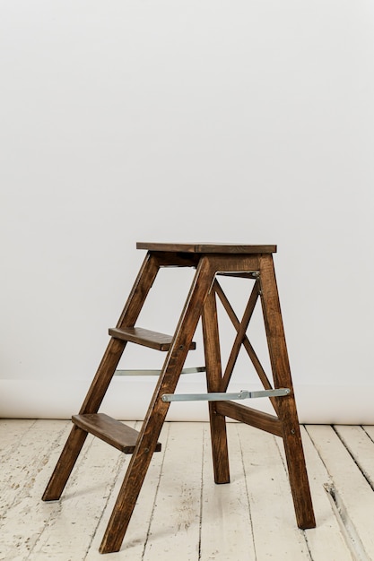 Silla de escalera de madera alta sobre pared fotográfica blanca sobre piso de madera blanca