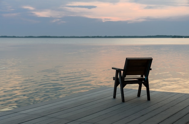 Silla de madera en un muelle de madera con vistas al lago tranquilo al atardecer horizonte