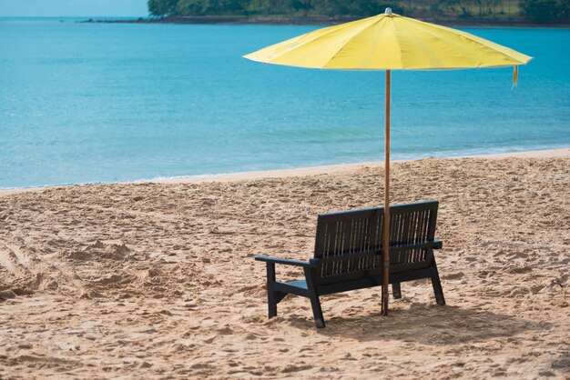 Silla de madera con sombrilla amarilla en la playa.