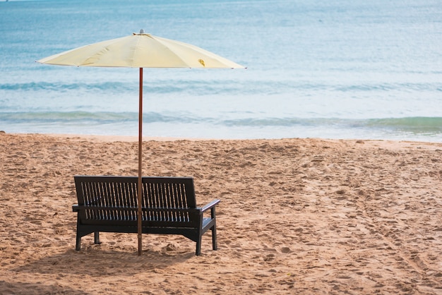 Silla de madera con sombrilla amarilla en la playa.