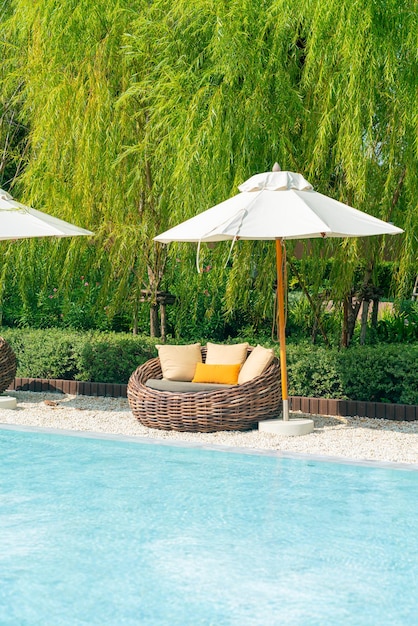 silla de patio al aire libre con almohada y sombrilla alrededor de la piscina - vacaciones y concepto de vacaciones