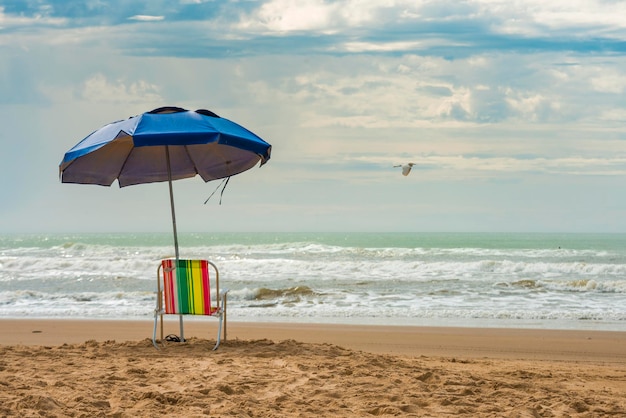 Silla de playa vacía con sombrilla azul con vistas al mar.